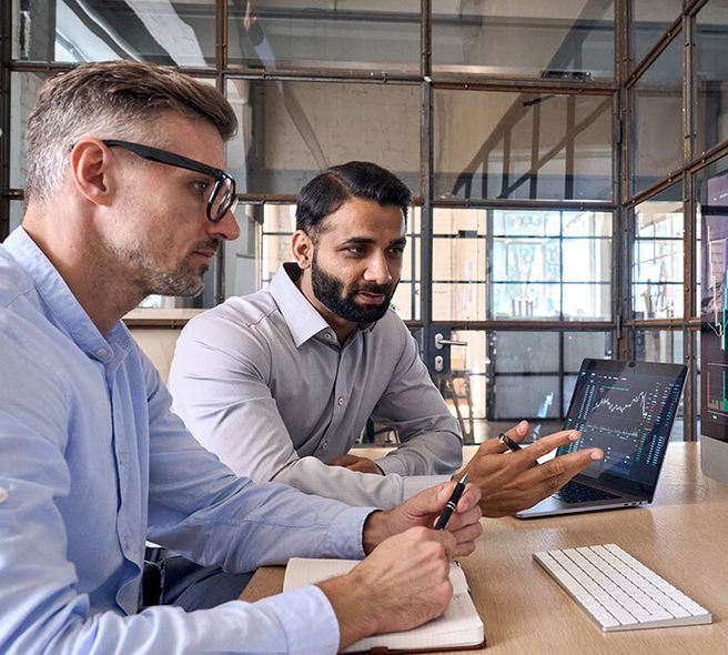 Confident woman in light-blue shirt, arms crossed in a glass-walled office, smiling with quiet assurance.